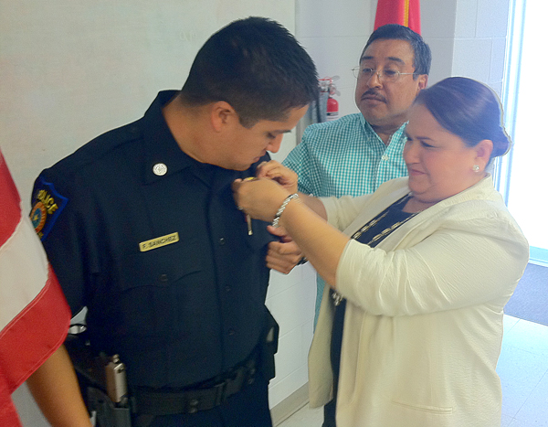 Norma Sanchez pins a badge on her son Officer Frank Sanchez while her husband looks on.